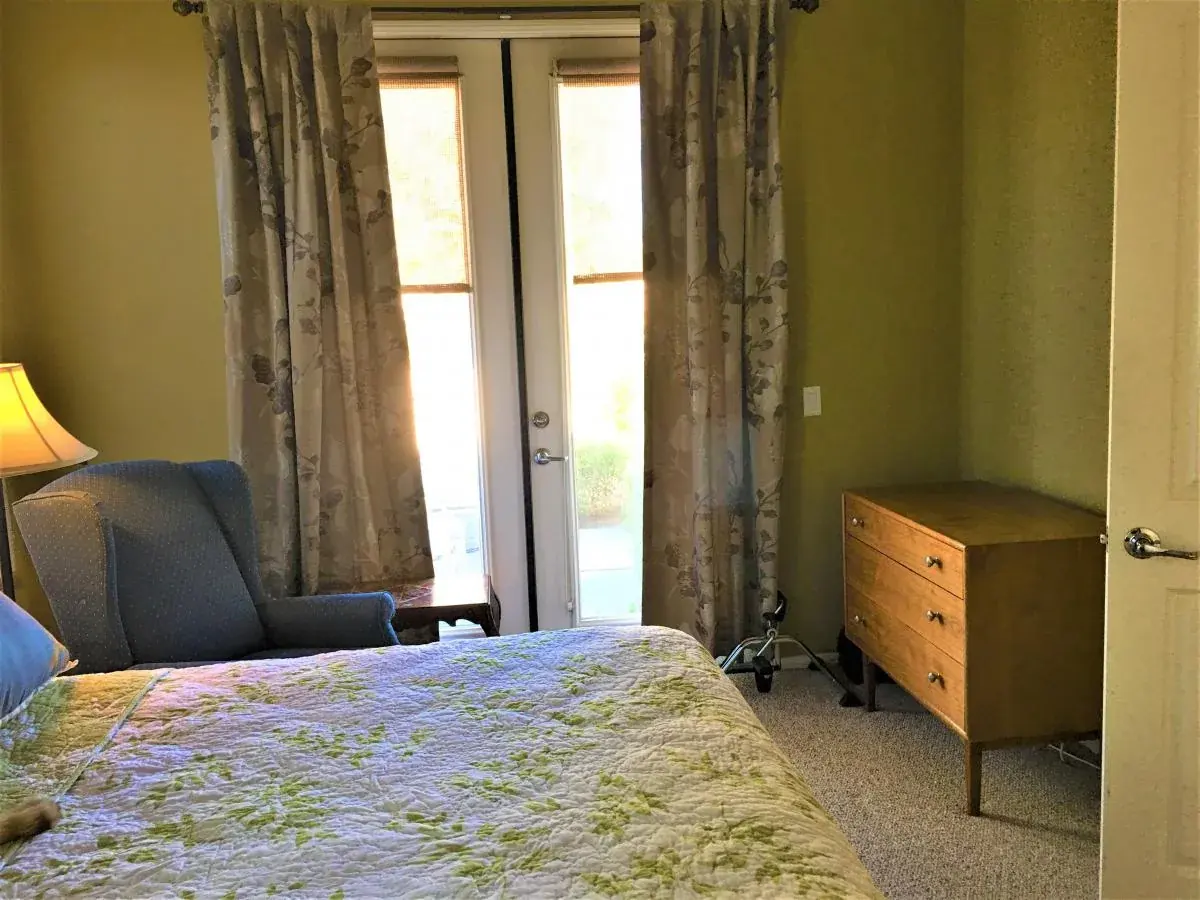 Another view of a furnished bedroom with a chair and French doors